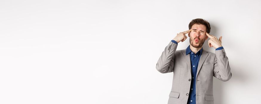 Distressed and tensed businessman pointing at head and complaining, feeling annoyed with situation blowing his mind, standing bothered on white background.