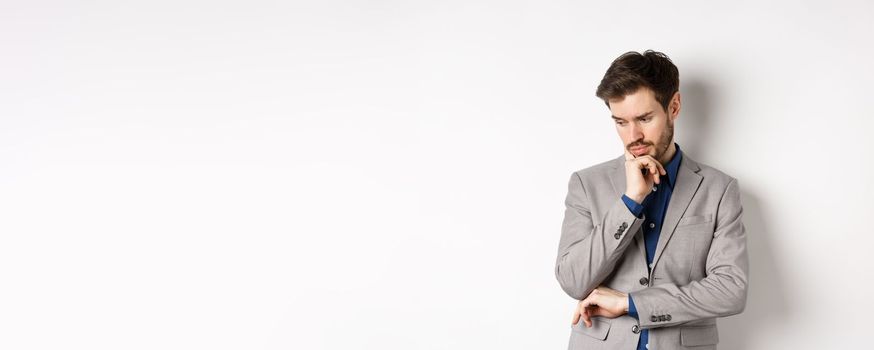 Thoughtful businessman in suit looking down and thinking, making decision, standing on white background.