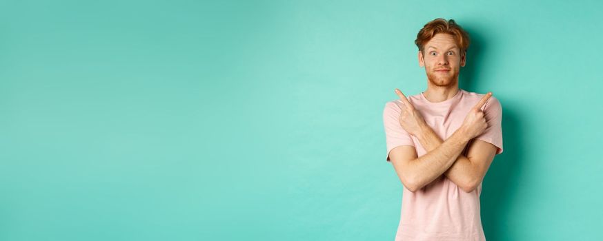 Attractive indecisive man in t-shirt cross hands and pointing sideways, showing two choices, need help with decision, standing over turquoise background.