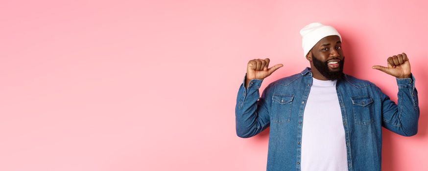 Confident Black bearded man in hipster beanie and denim shirt, pointing at himself with self-assured face, standing over pink background.