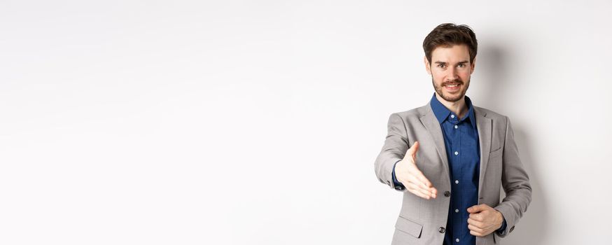 Confident businessman stretch out hand for business handshake and smiling, introduce himself on meeting, standing on white background.