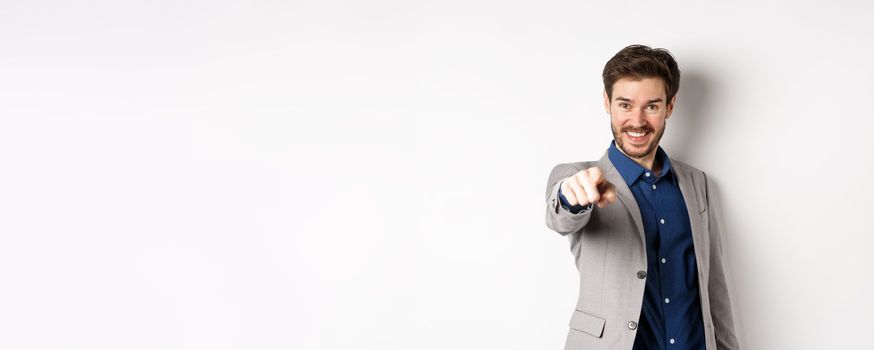 Its you. Smiling handsome manager in suit pointing at camera, choosing person and looking pleased, standing on white background.