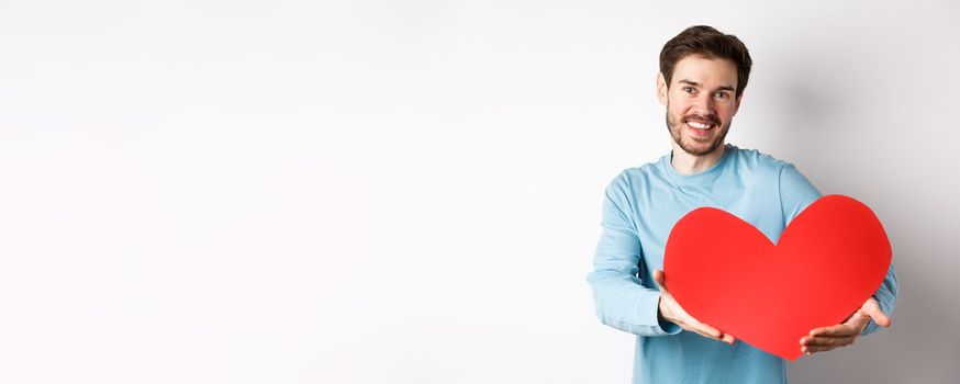 Happy gay man giving big red heart to his lover on valentines day, concept of romantic date and love celebration, standing over white background.