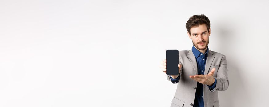 E-commerce and online shopping concept. Man demonstrated empty smartphone screen to you, showing phone display to introduce something, standing on white background.