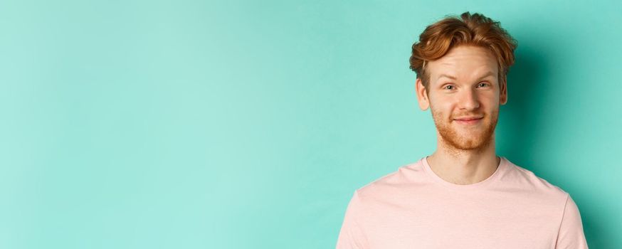 Close up of redhead bearded man looking pleased, nod in approval and smiling, standing in pink t-shirt against turquoise background.
