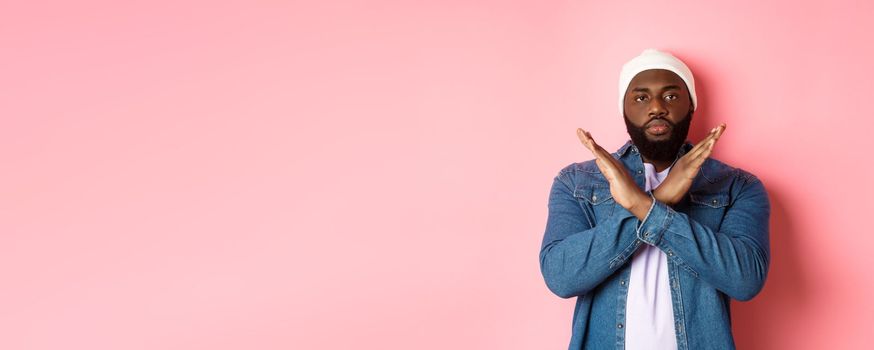 Serious african-american man saying no, showing cross to stop something bad, prohibit action, standing over pink background.