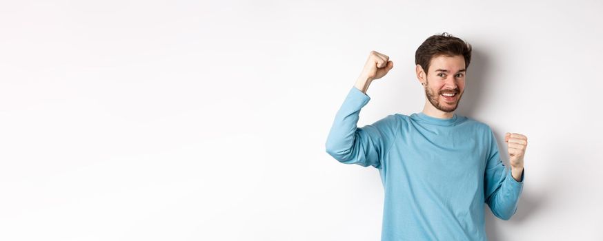 Happy bearded man celebrating victory, raising hands up and triumphing, winning prize and smiling with joy, standing over white background.