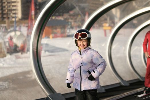 A girl on skis stands on a carpet ski lift in a tunel