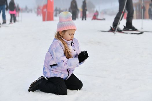A little girl making snowballs outdoors on winter day