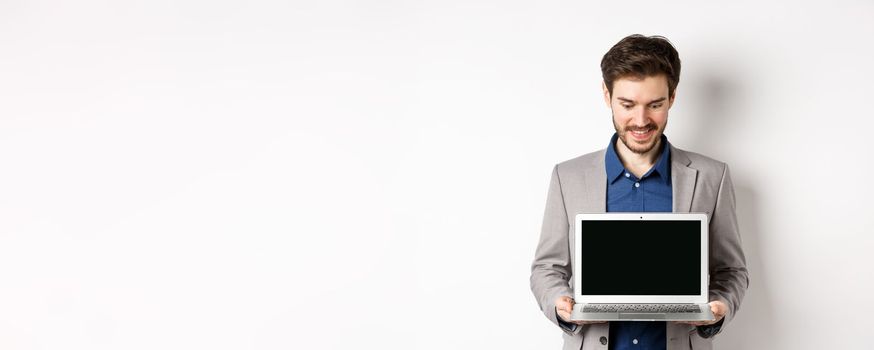 Handsome caucasian businessman in suit showing empty laptop screen, demonstrate promo, standing on white background.