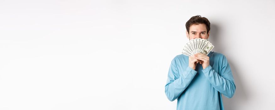 Cheerful shopper holding money for shopping, standing with dollars and smiling, standing over white background in casual clothes.