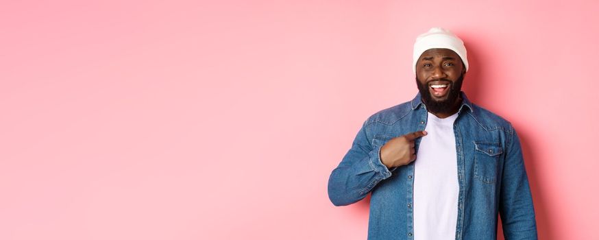 Offended and confused african-american man pointing at himself, staring at camera bothered, being accused, standing over pink background.