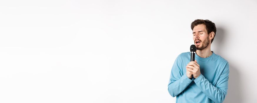 Young caucasian man singing song in microphone with carefree face, standing in karaoke over white background.