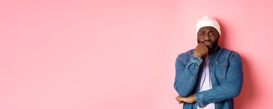 Young african-american man look with pity and concern at camera, frowning and feeling uneasy, standing over pink background.