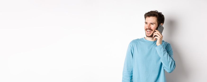 Technology concept. Joyful man enjoying phone call, talking on smartphone and smiling, standing in casual shirt over white background.