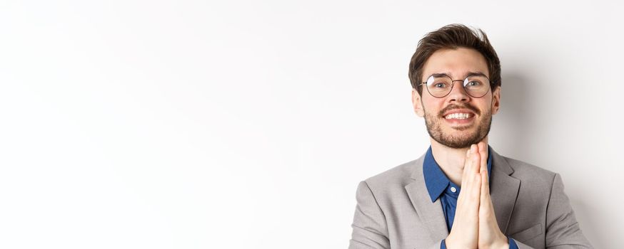 Close-up of happy thankful guy in glasses and suit showing gratitude, make namaste sign and smiling, standing on white background.