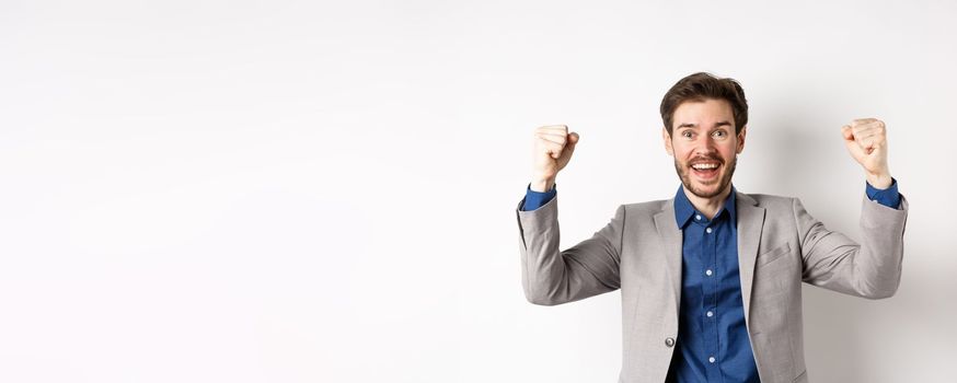 Happy man in suit raising hands up and chanting, watching sports game, winning in casino and celebrating, standing excited on white background.