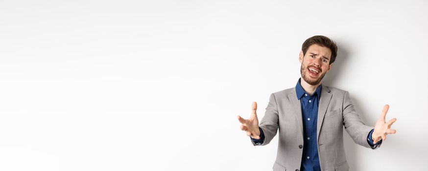 Desperate businessman stretch out hands and frowning disappointed, losing in game and feeling unfair, standing in suit on white background.