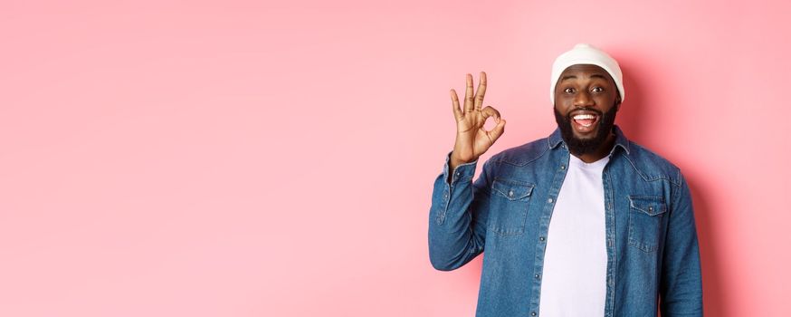 Happy smiling Black guy showing okay sign, approve and praise good offer, standing over pink background.