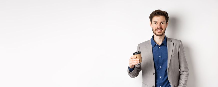 Smiling office worker in suit drinking coffee from paper cup, having break after work at cafe, standing against white background.