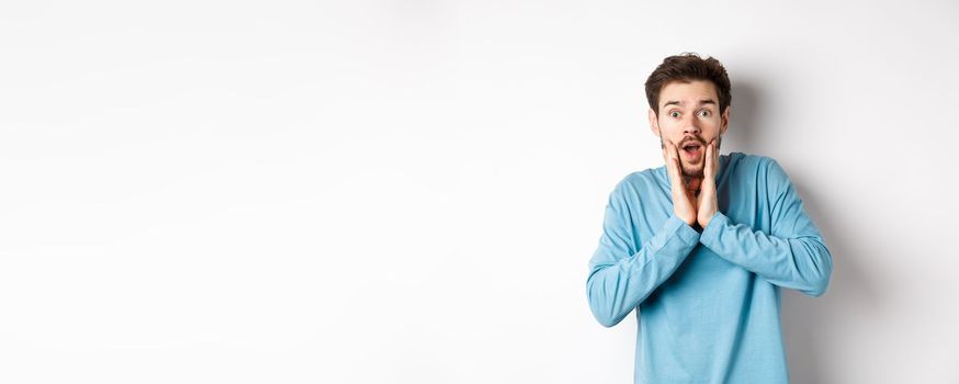 Image of handsome man gasping and staring at camera surprised, checking out awesome promo offer, standing over white background.