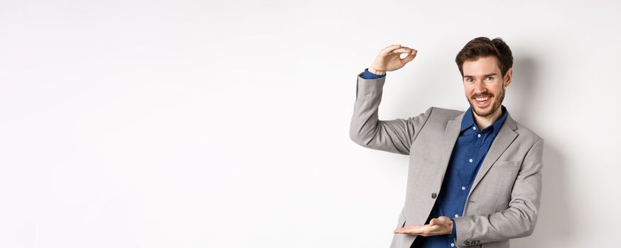 Successful businessman showing big size, shape large object and smiling pleased, standing on white background in suit.