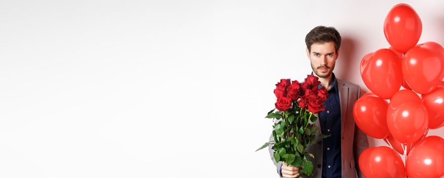 Macho man going on romantic date, looking confident at camera, holding gifts for lover on Valentines day, standing with heart balloons and red roses, white background.