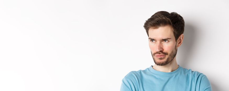 Close-up of disappointed bearded man, sulking and looking left with pensive face, standing upset over white background.