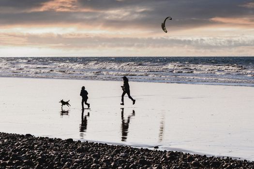 Mother daughter and dog running on the ocean coast at a sunset Selective focus