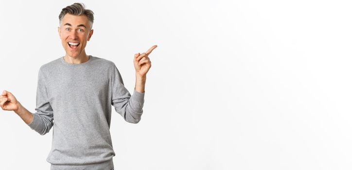 Image of handsome middle-aged man in grey sweater, showing two variants, pointing fingers sideways, demonstrating left and right copy space, standing over white background.