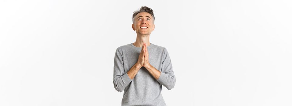 Image of nervous middle-aged man begging God, looking up and pleading for something, supplicating over white background.