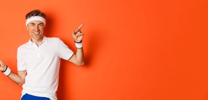 Concept of workout, sports and lifestyle. Portrait of active and healthy middle-aged guy in sportswear, smiling pleased, pointing fingers sideways and showing advertisements.