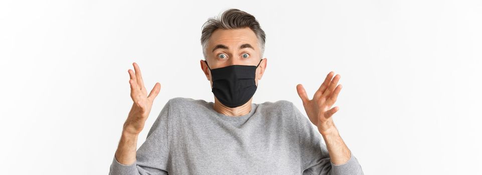 Concept of covid-19, social distancing and quarantine. Close-up of handsome middle-aged man in black medical mask, describe something amazed, looking fascinated at camera.