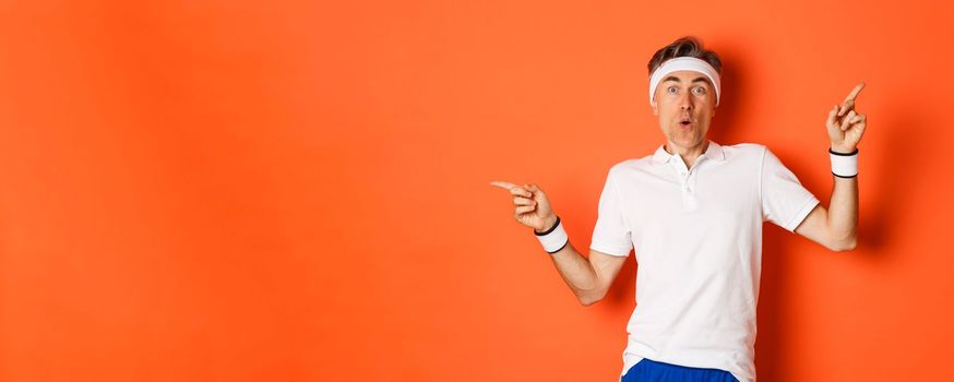 Concept of sport, fitness and lifestyle. Portrait of amazed and excited middle-aged male athlete, pointing fingers sideways, showing two variants, standing over orange background.