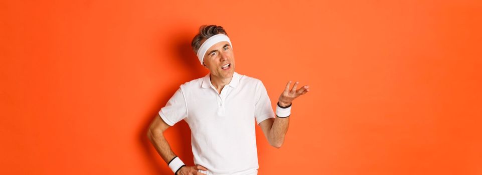 Concept of sport, fitness and lifestyle. Portrait of confused caucasian male athlete, asking question and looking bothered, cant understand something, standing over orange background.