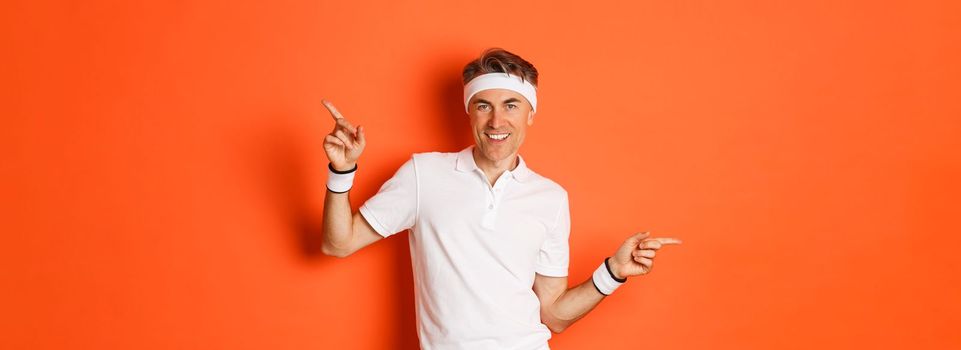 Concept of workout, sports and lifestyle. Portrait of active and healthy middle-aged guy in sportswear, smiling pleased, pointing fingers sideways and showing advertisements.