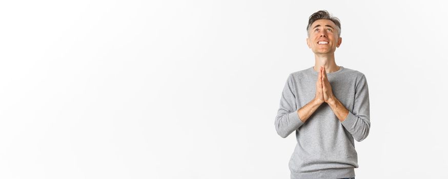 Image of nervous middle-aged man begging God, looking up and pleading for something, supplicating over white background.