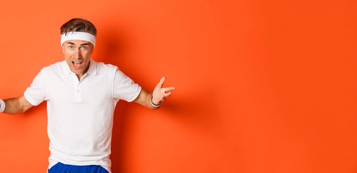 Concept of workout, sports and lifestyle. Portrait of confused middle-aged sportsman complaining, spread hands sideways and looking puzzled, cant understand something, orange background.