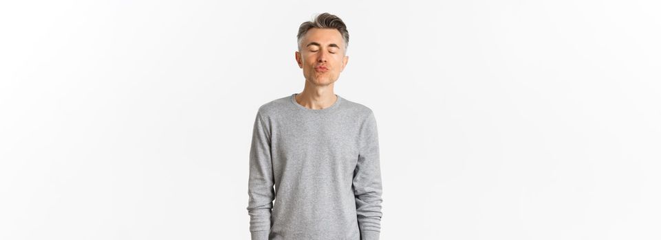 Image of lovely middle-aged guy waiting for kiss, close eyes and pouting, standing over white background.