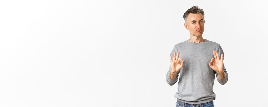 Image of impressed and satisfied middle-aged man, showing okay signs and nodding in approval, praise good choice, standing over white background.