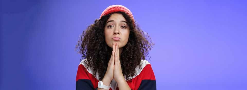 Lifestyle. Close-up shot of cute feminine girlfriend begging bring her favorite sweets holding hands in pray folding lips and gazing with angel innocent gaze at camera as asking favour over blue background.