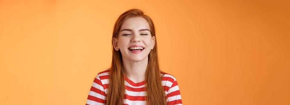 Sincere happy charismatic redhead girl smiling, close eyes enjoy warm summer sunbeams, laughing cheerful, feel relaxed rejoicing, show white teeth, good vacation concept, orange background.