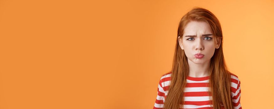 Childish offended cute redhead girl pouting, sulking upset, frowning, complain unfair situation, whining displeased, grimacing upset, act immature demand buy copy space orange background.