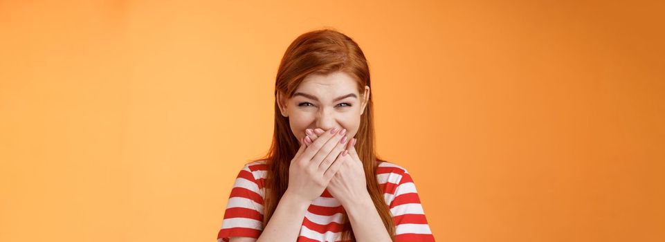 haha very funny. Silly tender cheerful redhead girl laughing, giggle hilarious joke, cover mouth press palms lips chuckling silent, mocking friend, stand upbeat orange background. Copy space