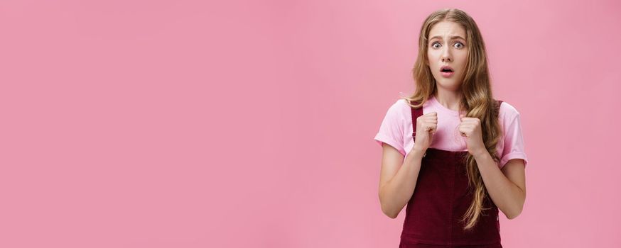 Young silly coward girl feeling insecure and scared stand up for herself raising clenched fists pressed to chest in self-defense open mouth in shock and fear looking scared at camera, being bullied. Body language concept