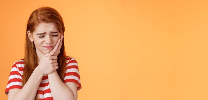 Close-up upset cute uneasy redhead girl suffer toothache, hold hand cheek frowning, close eyes awful tooth pain, have rotten teeth, decay problems, make dentist appointment, wait dental clinic.