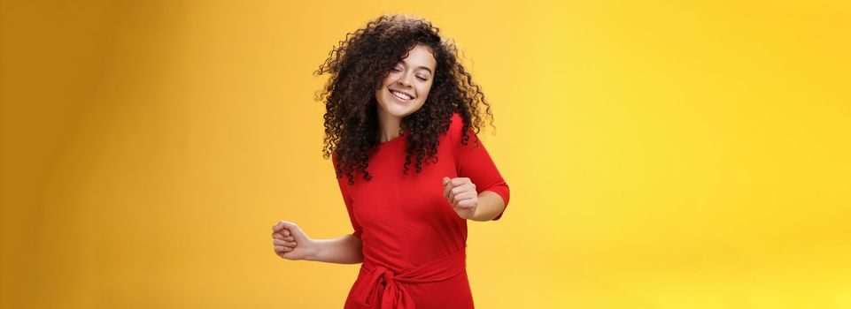 Carefree woman dancing on dance floor with close eyes and smile enjoying life feeling happy and joyful close eyes and making tender expression as moving to rhythm of music over yellow background. People, lifestyle and emotions concept