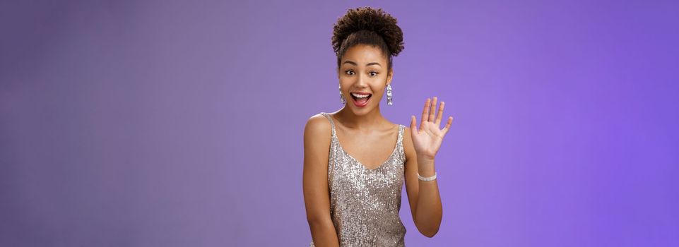 Friendly charming outgoing african-american woman see friend part nightclub smiling broadly say hi waving hello gesture greeting welcoming sociable, glad meet, standing joyful blue background.