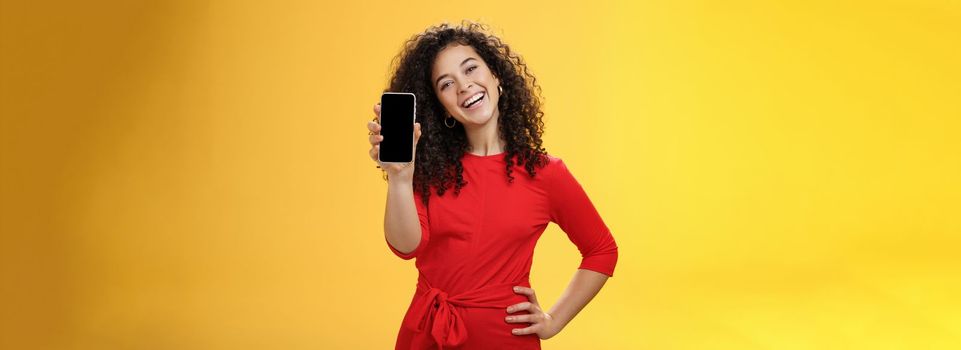 Carefree satisfied and happy attractive businesswoman presenting her best friend new mobile phone showing smartphone at camera laughing and smiling joyfully delighted with new purchase. Emotions and technology concept