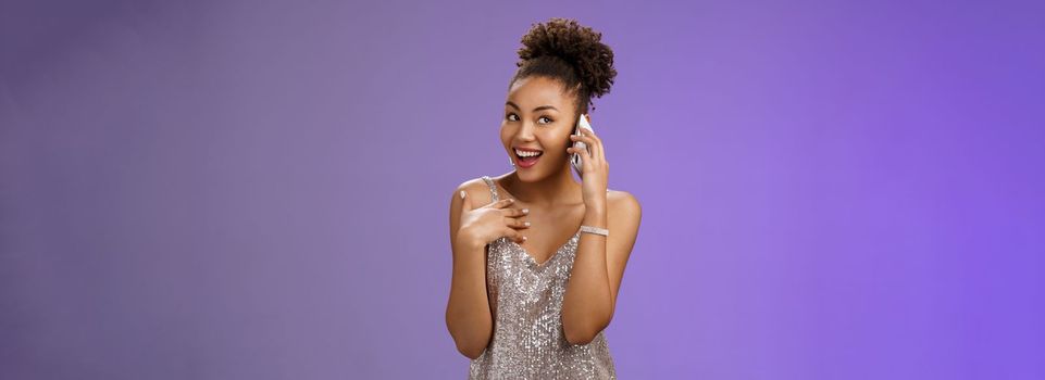 Attractive wealthy talkative pleased african american girl discuss silly things calling friend smartphone speaking phone gesturing pointing herself bragging during phonecall standing blue background.